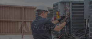 Stock photo of man wiring outdoor HVAC unit.
